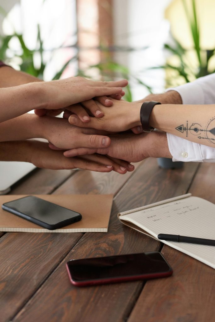 Accompagnement des Dirigeants Hands from a diverse team stack on a table symbolizing unity and teamwork in a modern office setting.